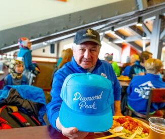 senior man holds up blue diamond peak hat