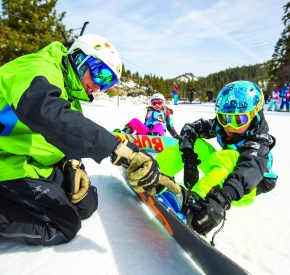 snowboard instructor kneels to teache boy about snowboard edge