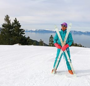 skier in teal retro ski onesie poses at the top of crystal ridge at diamond peak with lake tahoe views