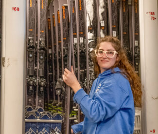 female employee in rental shop hangs up skis