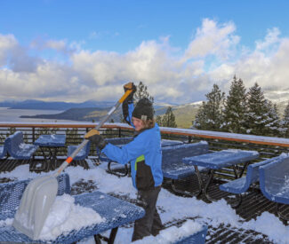 male employee clears snow off the deck with lake tahoe views