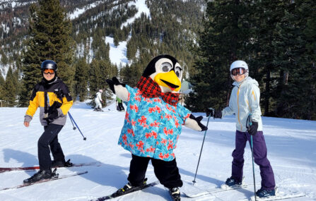 diamond peak's mascot penguin pete in a tropical shirt on the slopes with a couple of skiers smiling